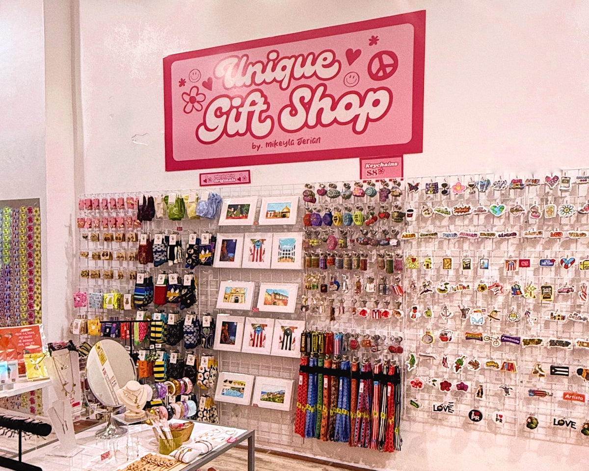 A retail gift shop display with a large pink sign reading 'Unique Gift Shop' above acrylic wall racks filled with colorful accessories, bracelets, pins, and small gift items.